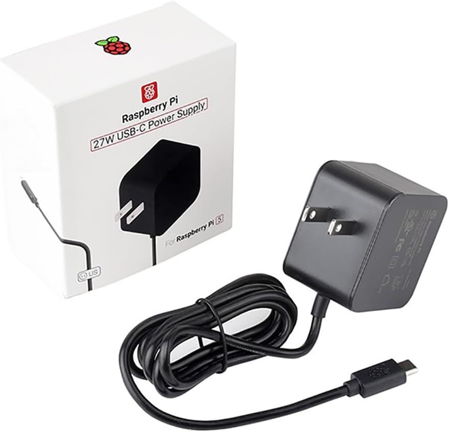 Schwarzes Raspberry-Pi-27-W-USB-C-Netzteil mit aufgewickeltem Kabel vor seiner weißen Verpackung mit Aufschrift „27W USB-C Power Supply“.