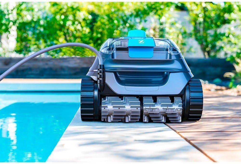 Frontansicht des grau-blauen Roboters mit Kabel und zwei Helix-Buersten auf dem Beckenrand neben dem Pool.