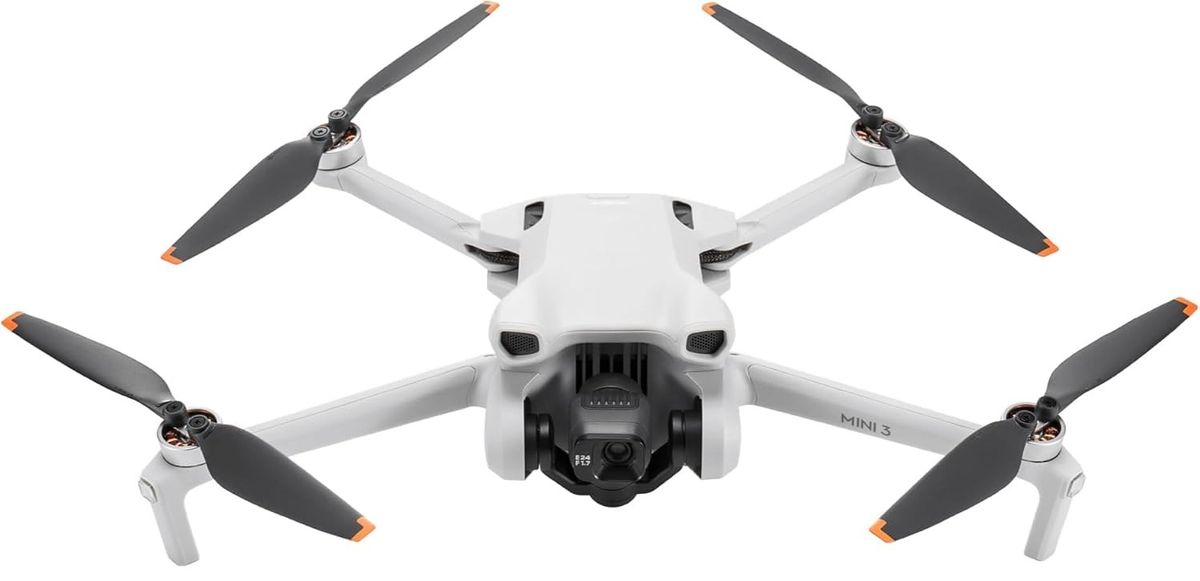 Hellgraue DJI Mini 3 mit ausgeklappten Armen, orangefarbenen Propellerspitzen und Kamera-Gimbal in Frontansicht vor weißem Hintergrund.