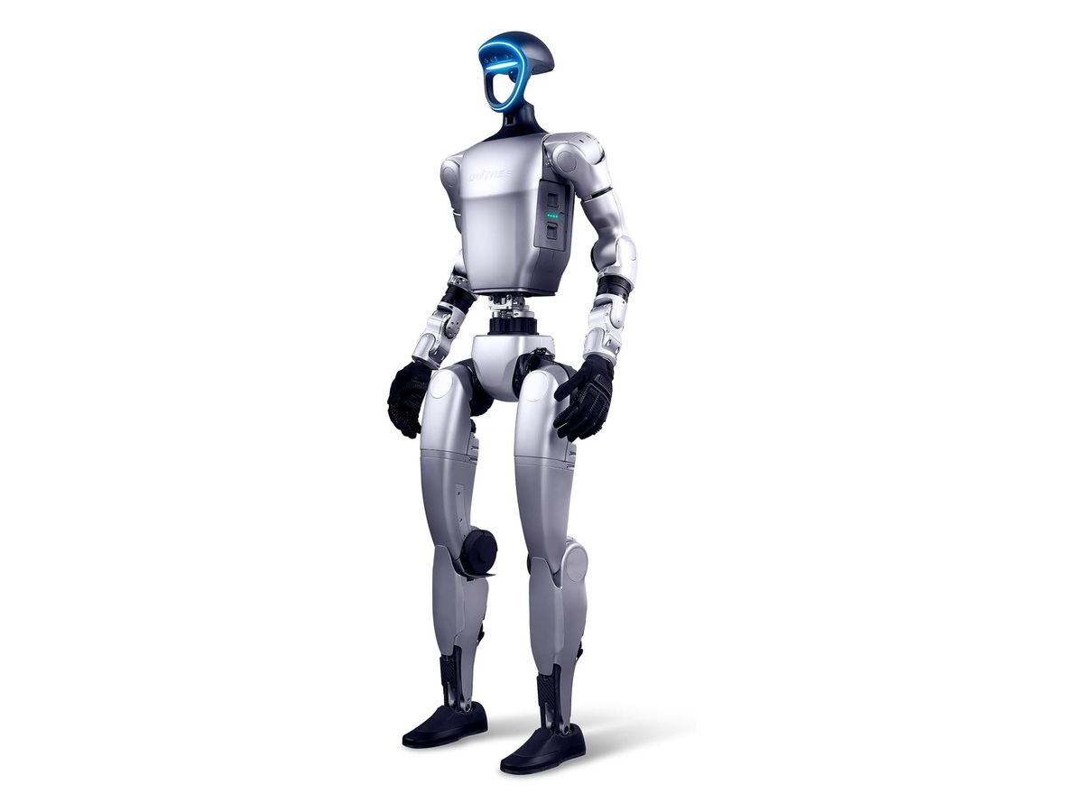 Silberner humanoider Roboter Unitree G1 steht leicht schräg von vorn, mit blau leuchtendem Ring am Kopf, Akku-Statusanzeige an der Rumpfseite und schwarzen Handschuhen.