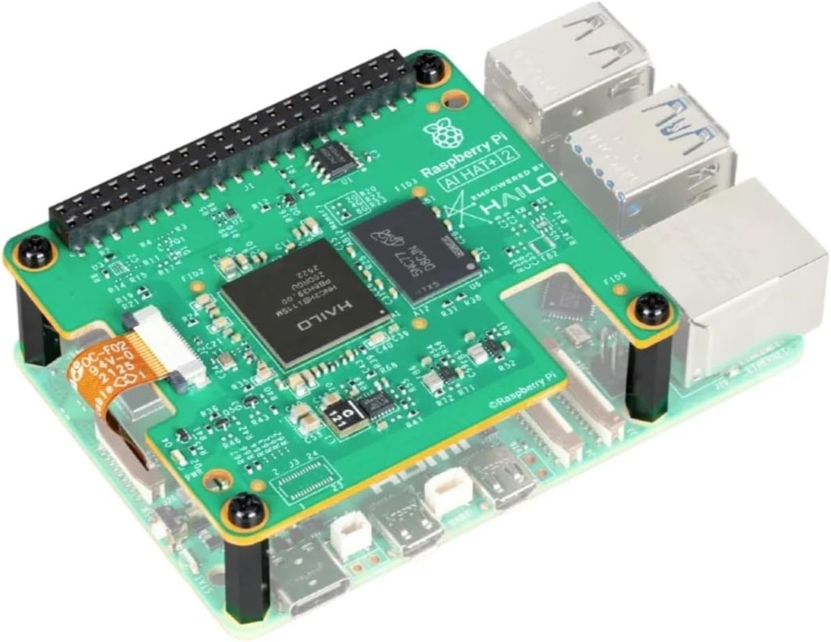 AI HAT+ 2 mit schwarzem Hailo-10H-Chip und daneben liegendem Speicherchip, auf einem Raspberry Pi 5 montiert.