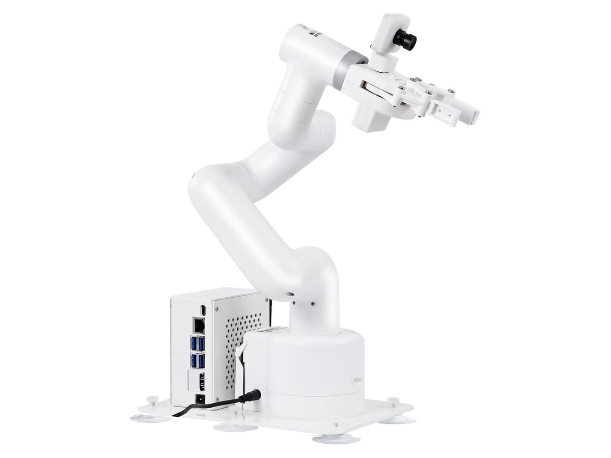 Weißer sechsgliedriger Roboterarm mit Kamera und Parallelgreifer auf weißer Grundplatte, daneben ein weißes Metallgehäuse mit USB- und Netzwerkbuchsen.
