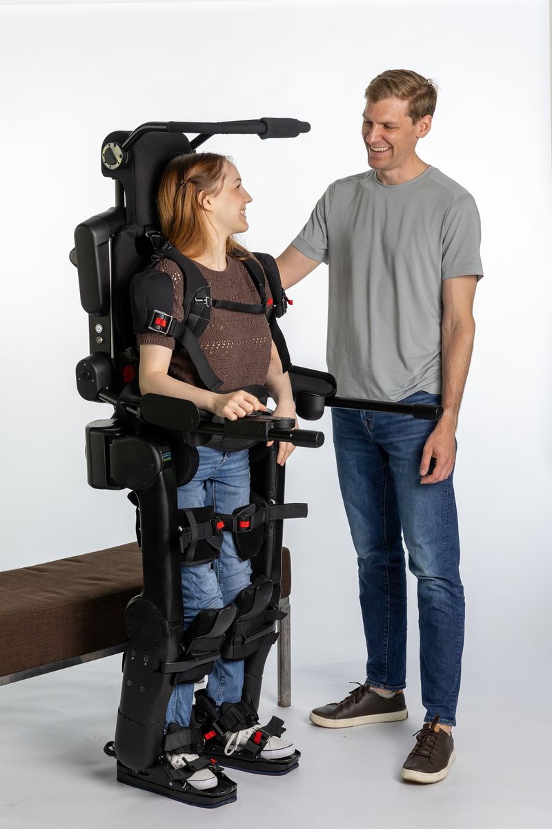 Eine Frau im Exoskelett Eve steht aufrecht und spricht mit einem neben ihr stehenden Mann auf Augenhöhe