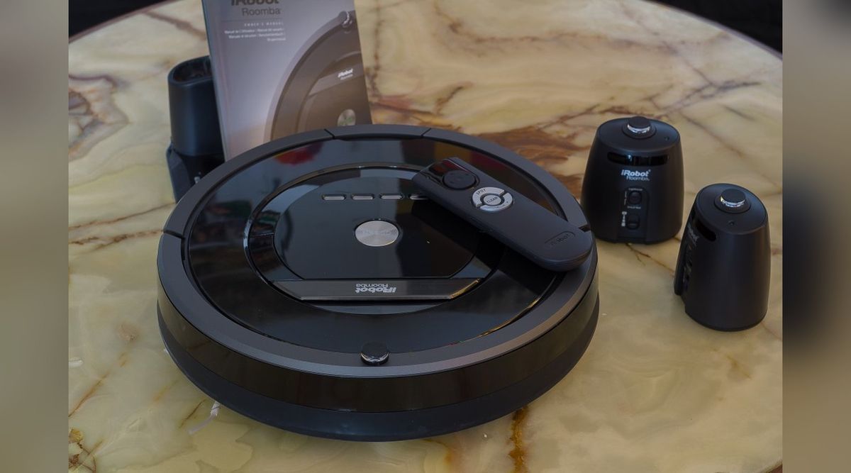 Schwarzer Saugroboter iRobot Roomba 880 mit Fernbedienung auf einem Marmortisch, daneben zwei Leuchtturm-Module, Ladestation und Bedienungsanleitung