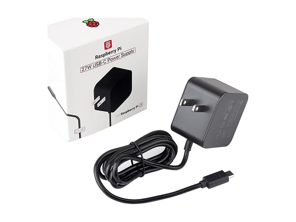 Schwarzes Raspberry-Pi-27-W-USB-C-Netzteil mit aufgewickeltem Kabel vor seiner weißen Verpackung mit Aufschrift „27W USB-C Power Supply“.