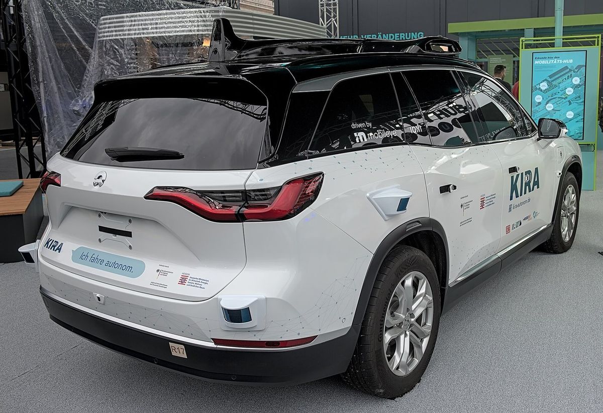 Weißes SUV mit schwarzem Dach und großem Sensoraufbau von hinten schräg, Aufschrift „KIRA“, „Ich fahre autonom.“ und „driven by mobileye“, an Heck und Seite kleine Sensorgehäuse