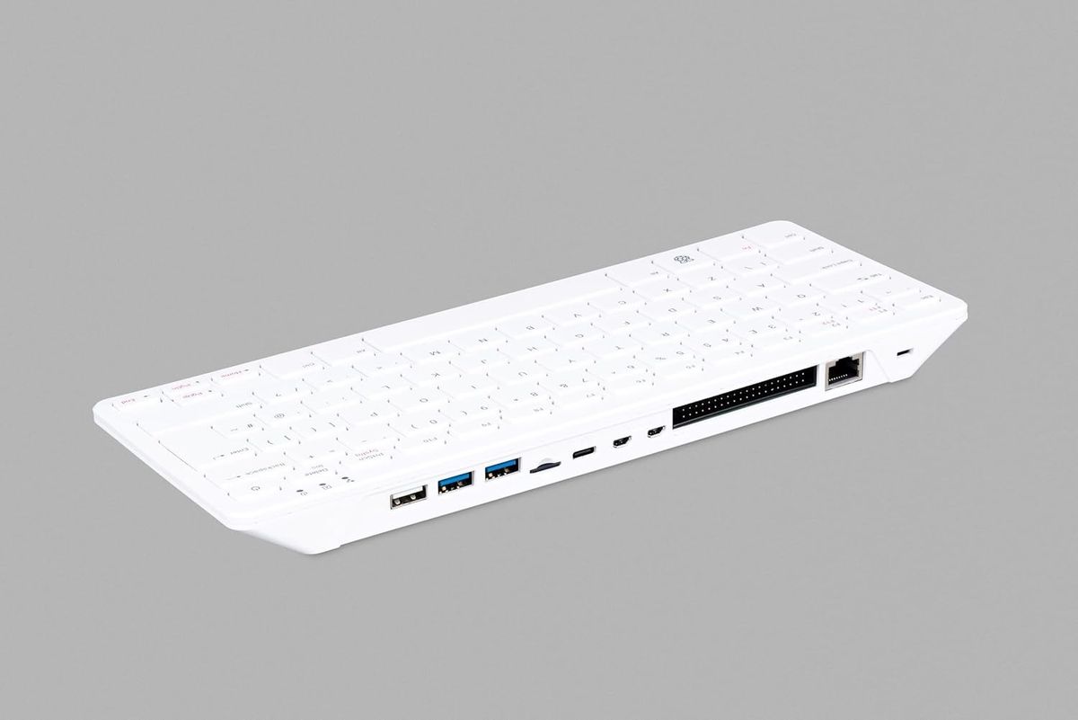 Weißer Raspberry Pi 500 schräg von hinten mit Anschlussleiste aus USB-Ports, microSD-Slot, USB-C, zwei Micro-HDMI-Buchsen, GPIO-Leiste und Ethernet; abgebildet ist eine Tastatur mit englischem Layout.