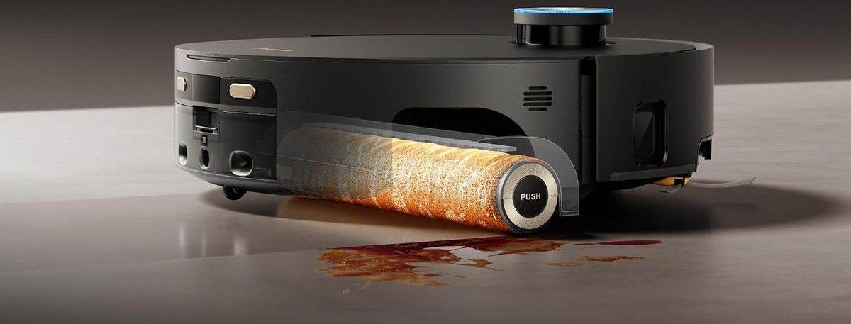 Schwarzer Saugroboter in Seitenansicht auf hellem Hartboden; die transparent dargestellte orangefarbene Wischwalze mit der Aufschrift PUSH rollt über einen rotbraunen Fleck.