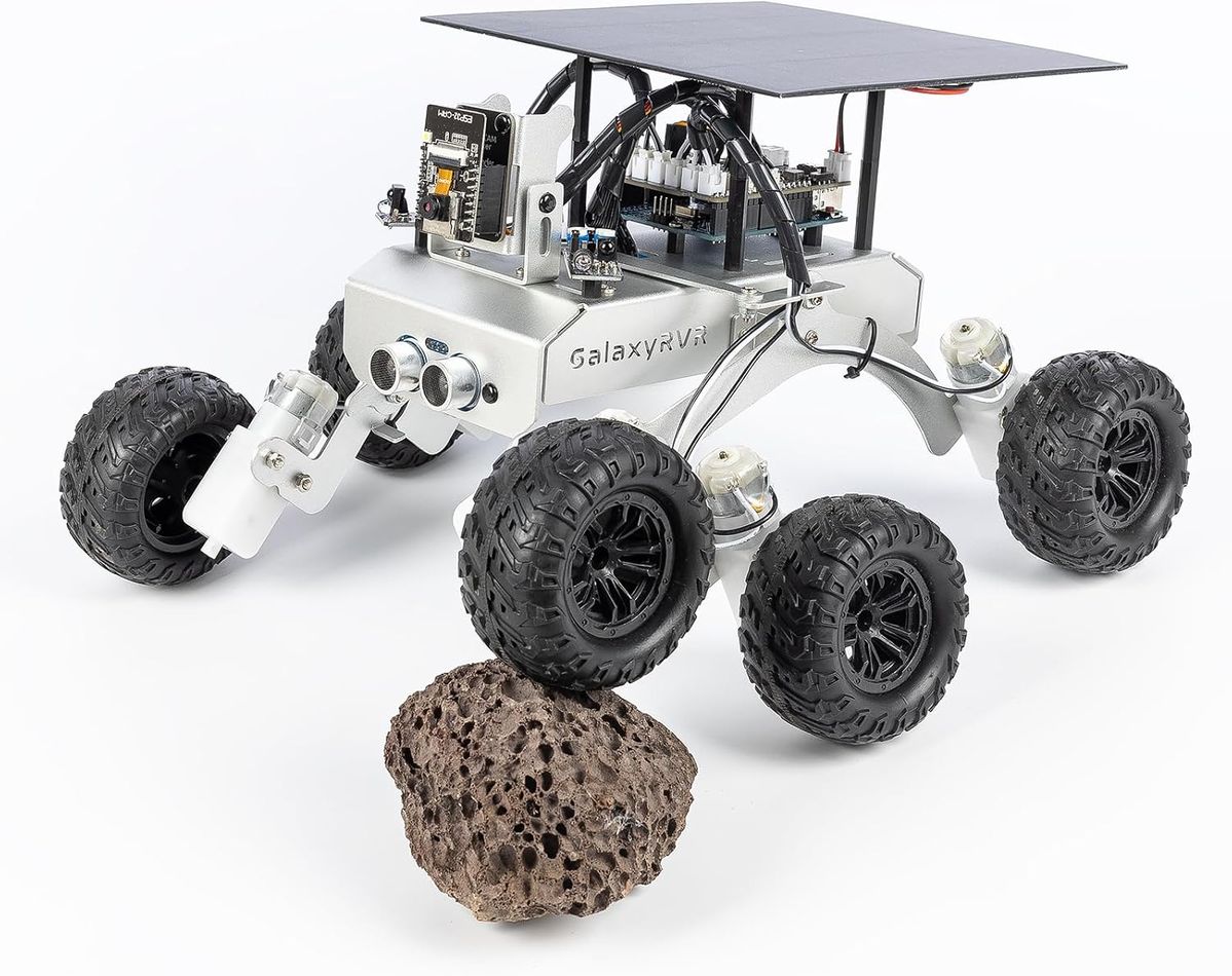 Silberner Mars-Rover GalaxyRVR mit sechs Geländereifen, Solarpanel auf dem Dach und ESP32-Kamera, ein Rad steht auf einem Lavastein.