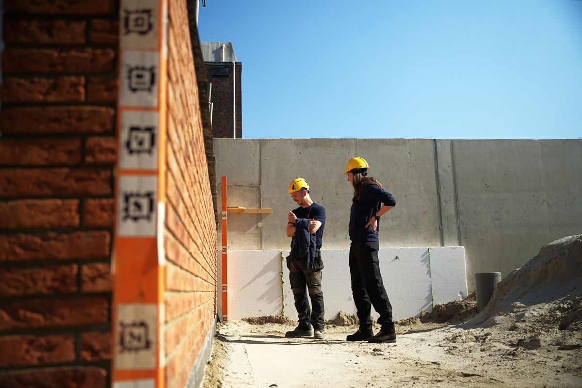 Zwei Bauarbeiter mit Helmen an einer entstehenden Klinkerwand auf einer Monumental-Baustelle