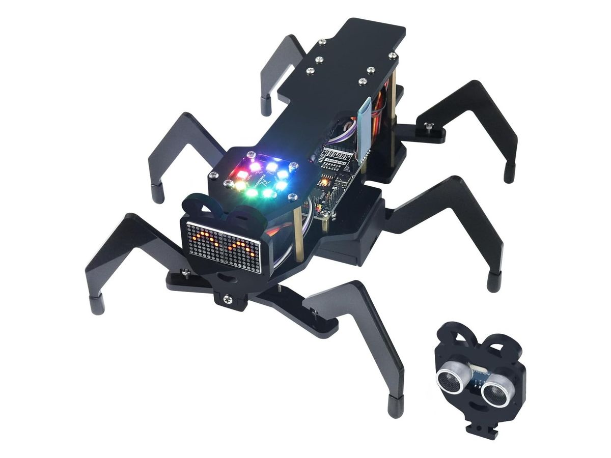 Sechsbeiniger Ameisenroboter aus schwarzem Acryl mit LED-Matrix und bunt leuchtendem RGB-LED-Ring am Kopf, daneben der zweite Kopf mit Ultraschallsensor.