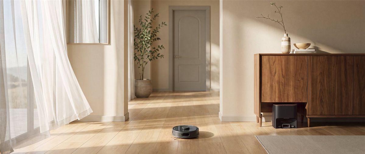 Schwarzer SwitchBot K11+ Pro faehrt ueber einen hellen Holzboden, seine Absaugstation steht unter einem Sideboard.