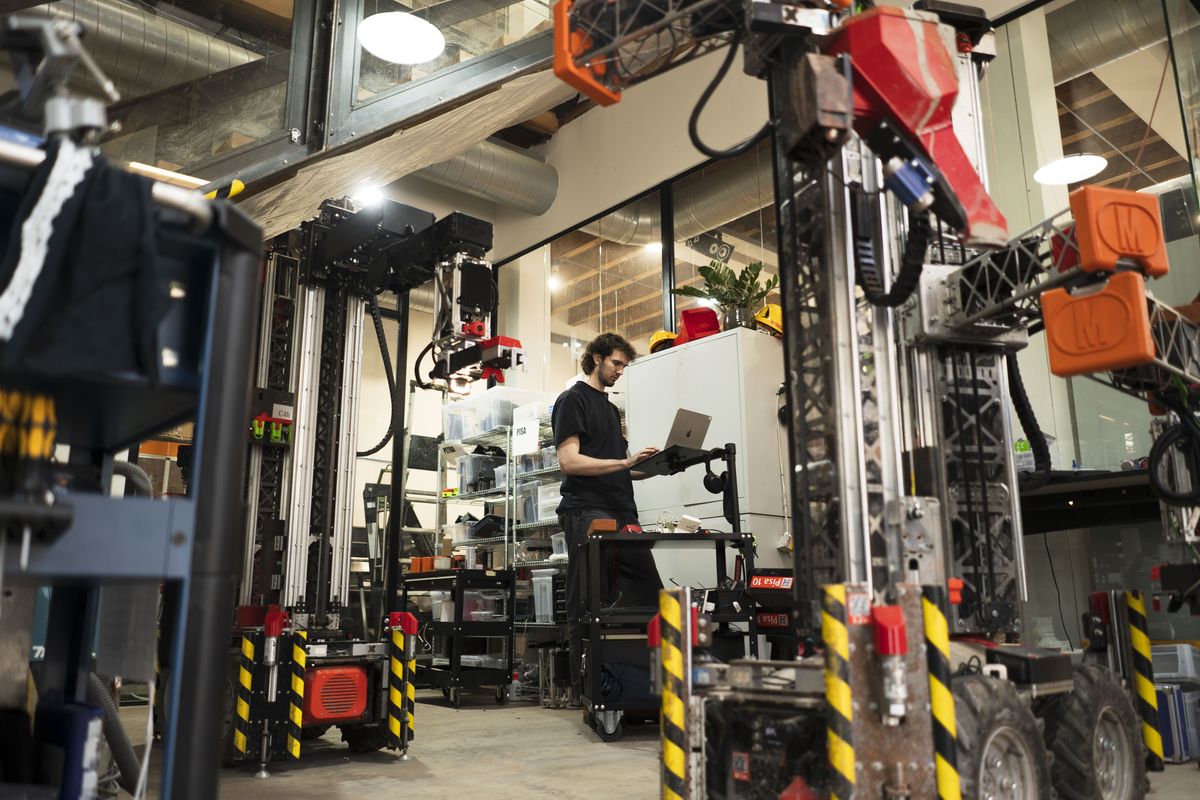 Werkstatt von Monumental in Amsterdam mit mehreren Maurer-Robotern und einem Entwickler am Laptop